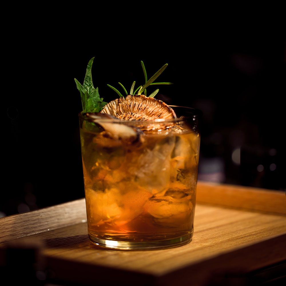Das Bild zeigt einen Whiskey in einem Glas. Er sieht orange aus und ist mit Kräutern garniert.