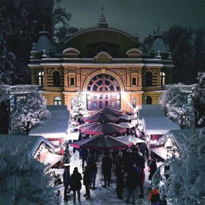 Weihnachtsmarkt mit beleuchteten Ständen und Besuchern vor dem schneebedeckten Kurhaus Göggingen bei Nacht (C) Oliver Pollen