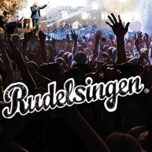 Menschenmenge mit erhobenen Händen vor einer Bühne, auf der ein Mann mit Mikrofon steht, darüber der Schriftzug 'Rudelsingen'
